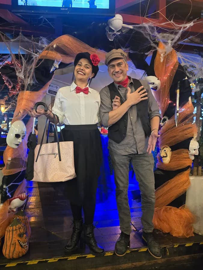 Dos personas disfrazadas posan sonriendo frente a un decorado de Halloween con telarañas, calaveras y tela naranja, dentro del mercado.