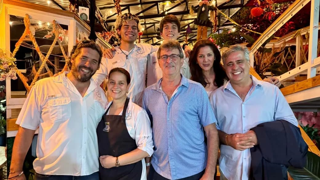 Siete personas del equipo posan juntas y sonriendo frente a la escalera del mercado, decorada con flores y luces.